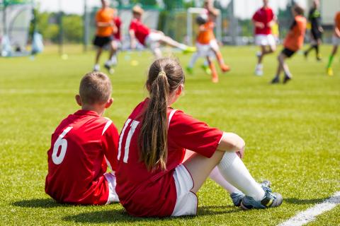 Two students in red soccer jerseys sitting out a soccer game.